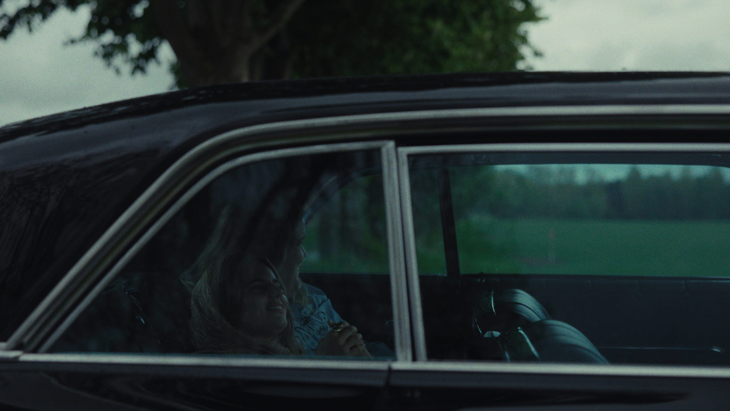 A woman seated in a car, muted green tones