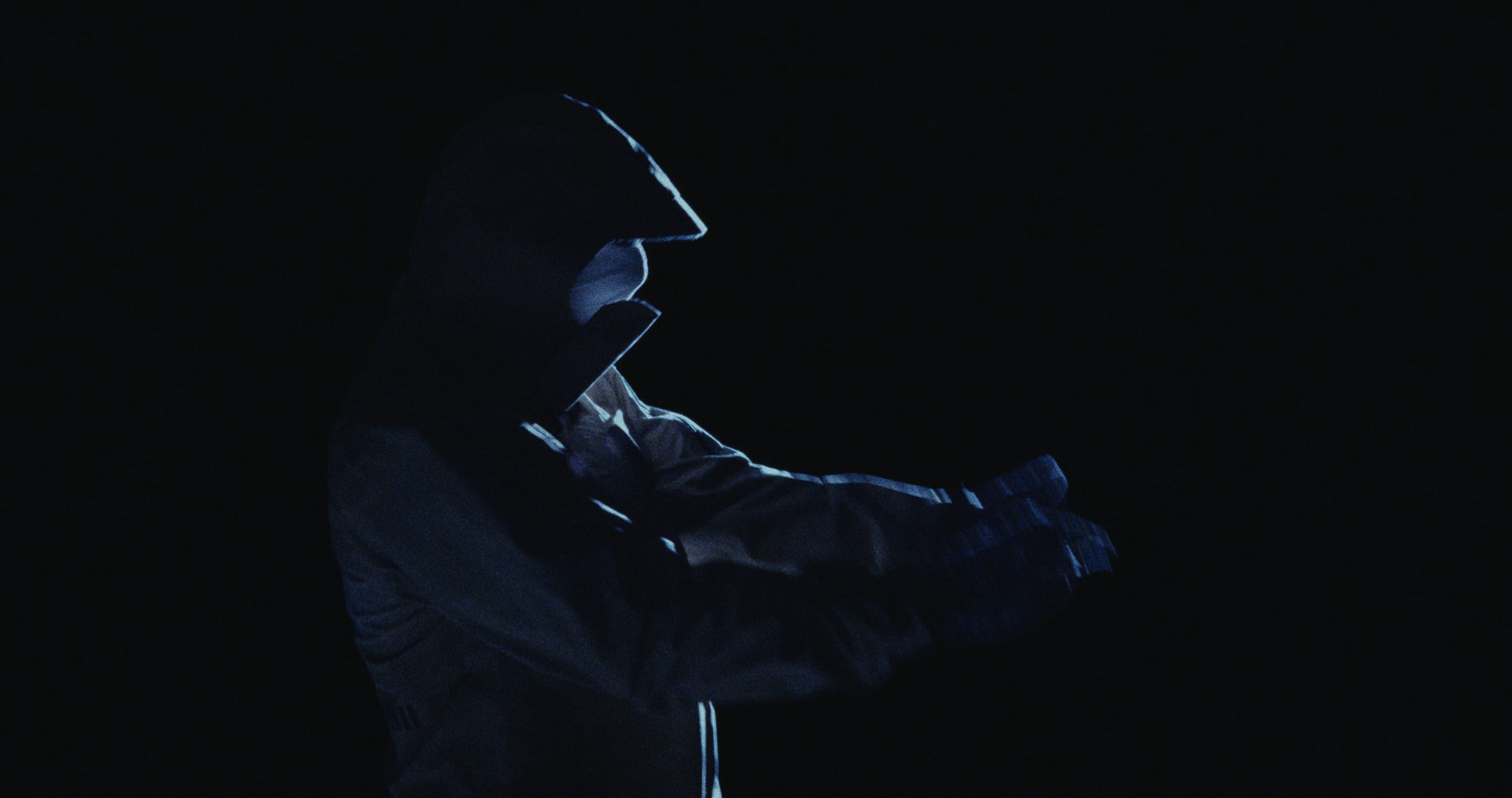 A hooded figure in silhouette, arms outstretched in the dark