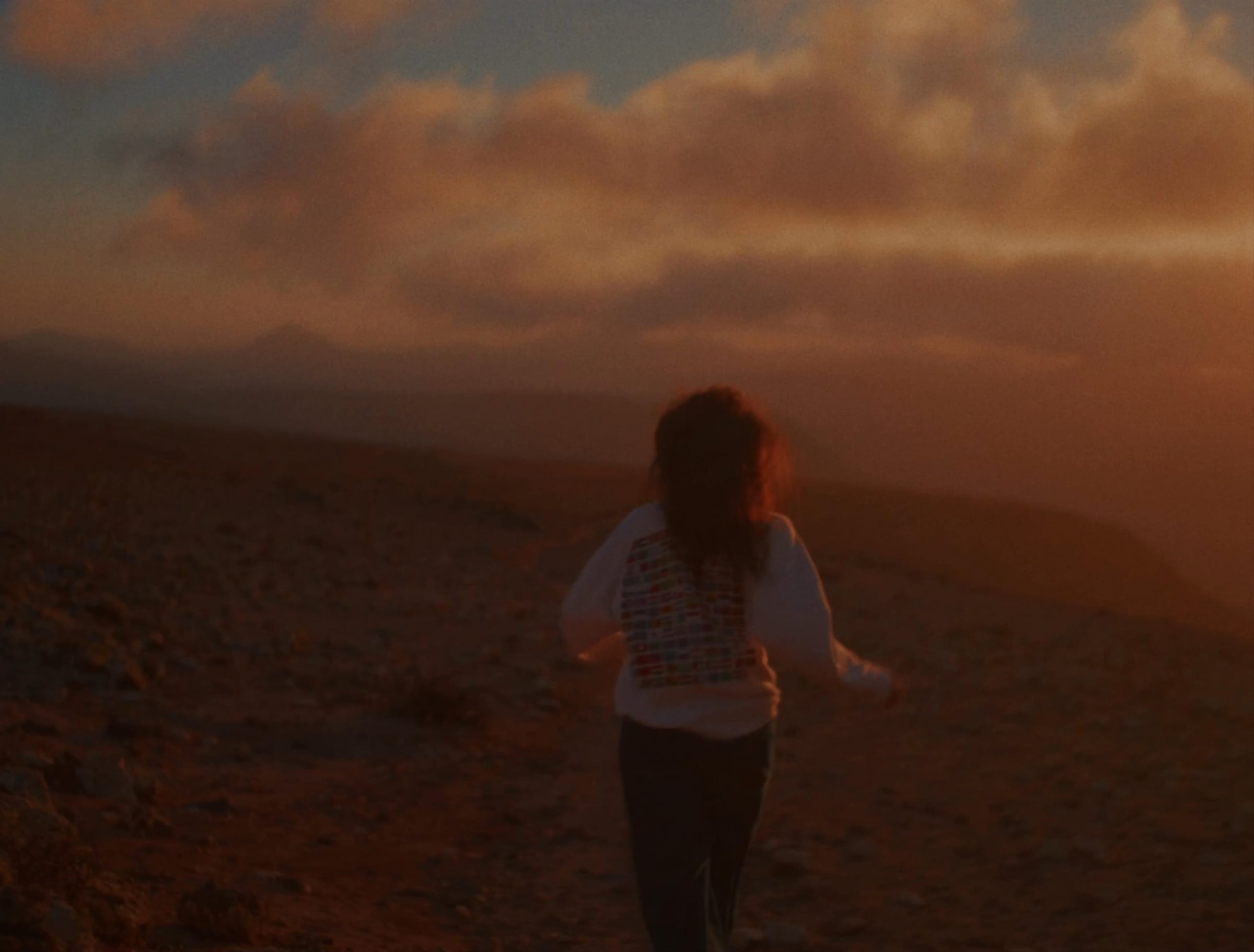 A woman walking away across bare hills at dusk